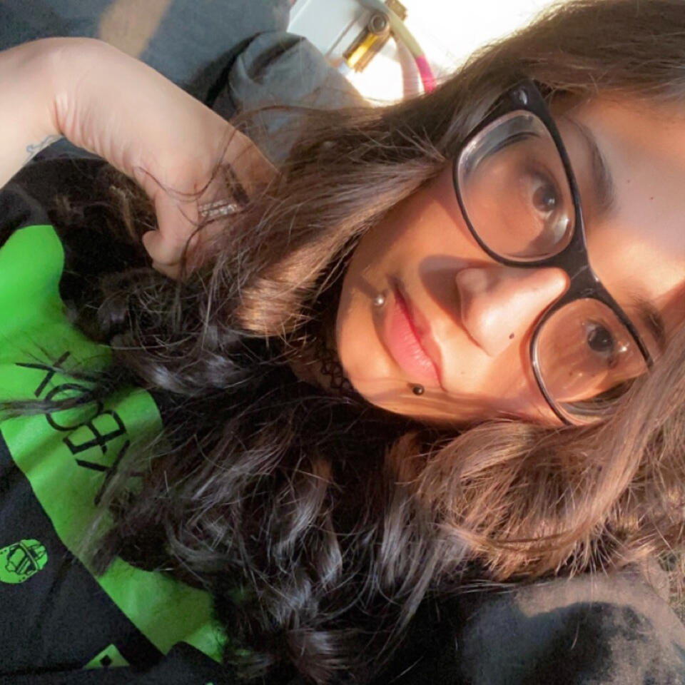 Shan's Profile Picture. An image of Beersnack_. They have shoulder-length brown hair, brown eyes behind black glasses and snake bite piercings. They are wearing a black and green t-shirt.