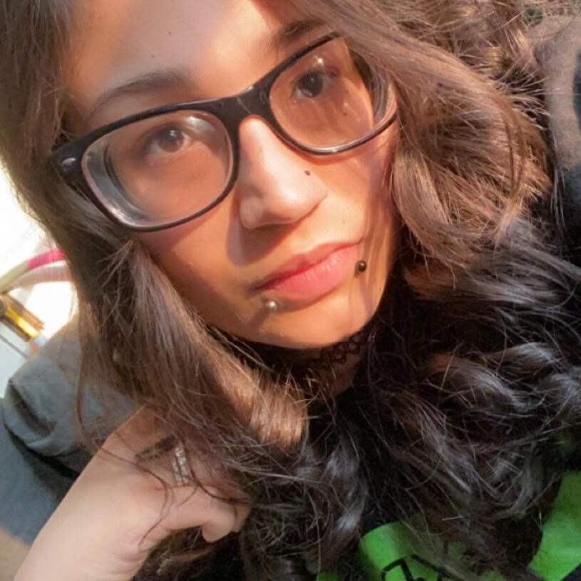 Shan's Profile Picture. An image of Beersnack_. They have shoulder-length brown hair, brown eyes behind black glasses and snake bite piercings. They are wearing a black and green t-shirt.